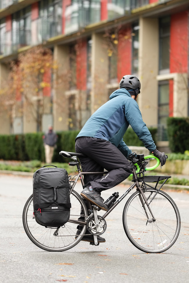 Man biking in the rain with the Two Wheel Gear Duffle bag on the rack of his bike.